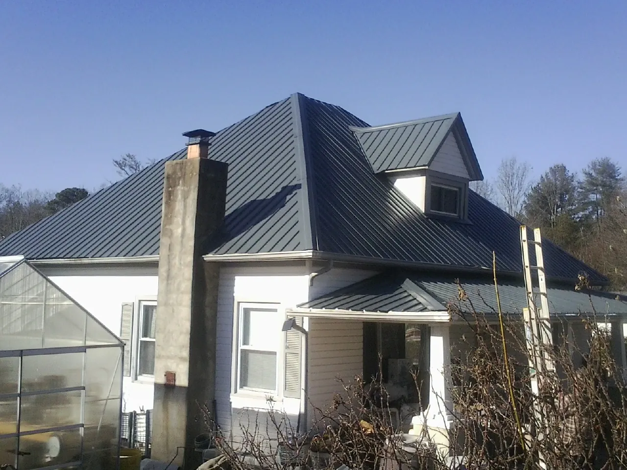 Dark blue standing seam metal roof on a white farmhouse with dormer — Slate & Tile Roof Repair by Roofing Brothers in Coral
