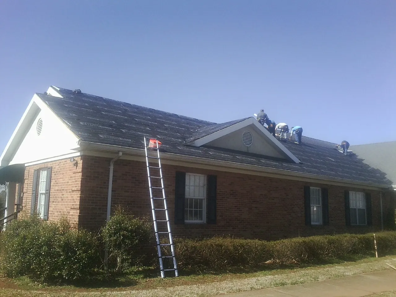 Crew tearing shingles off a brick ranch roof with a ladder set — Metal Roof Repair work by our crew in Coral
