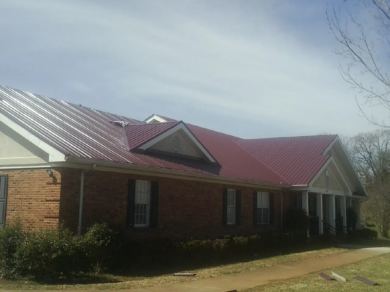 Red metal roof with gabled entries on a long brick building, from a Hail Damage Roof Repair job in Coral