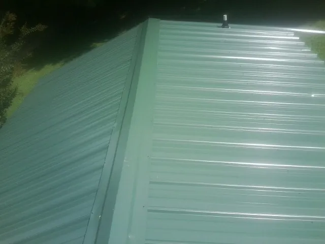 New green metal panels meeting at the ridge of a roof — Flat Roof Repair work by our crew in Coral